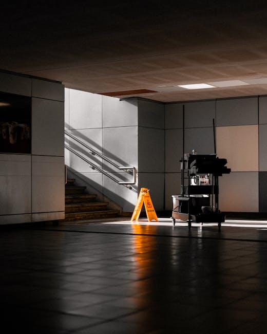 An area of a commercial indoor space featuring tiled flooring that appears clean and polished, with sunlight streaming through an opening, casting shadows on the floor. In the background, there is a s