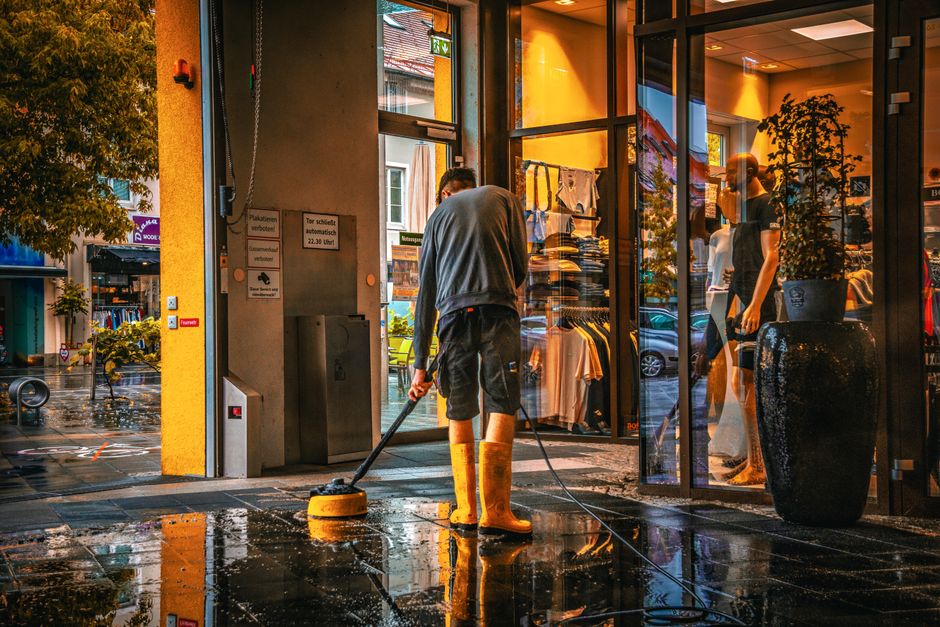 An area of a commercial indoor space featuring tiled flooring that appears clean and polished, with sunlight streaming through an opening, casting shadows on the floor. In the background, there is a s